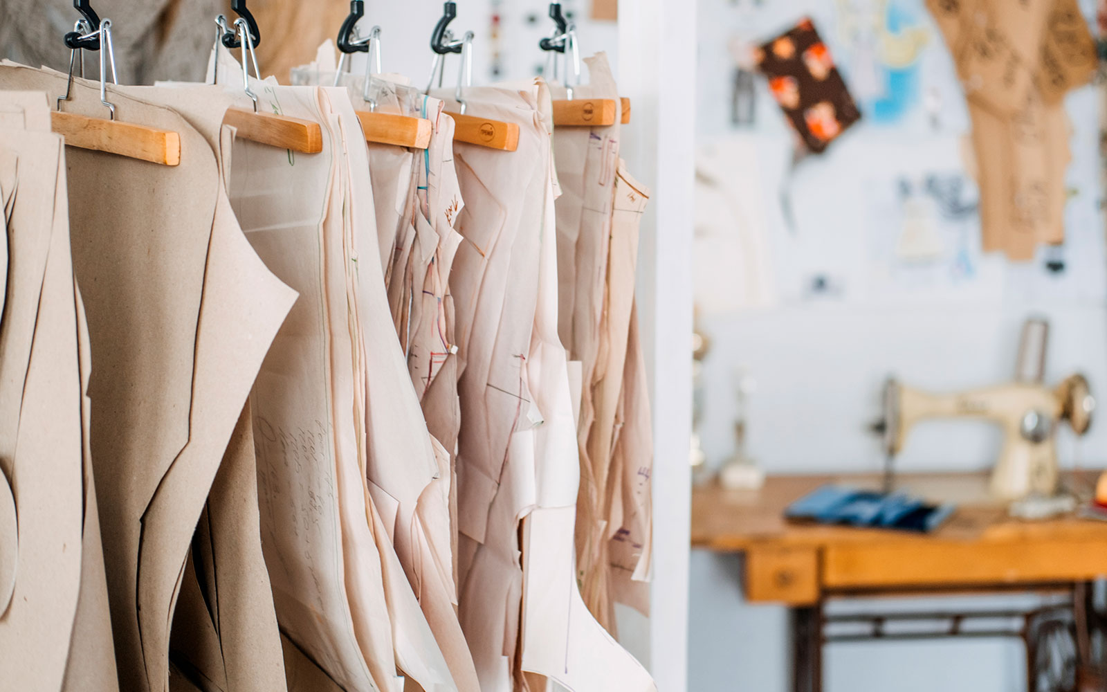 Patrones de papel colgados de perchas de madera, con una máquina de coser al fondo